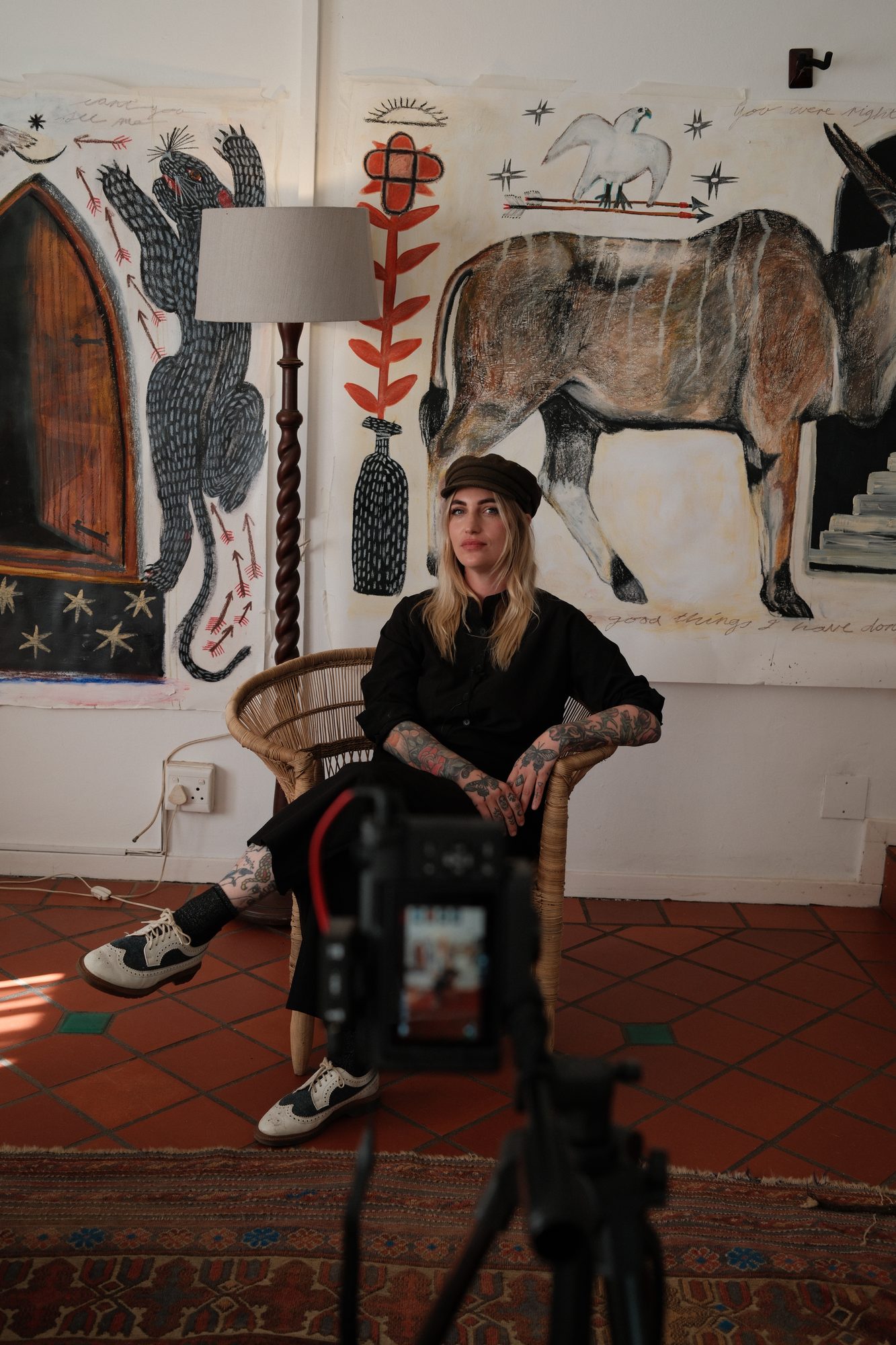 An artist in conversation in her studio, with paintings behind her