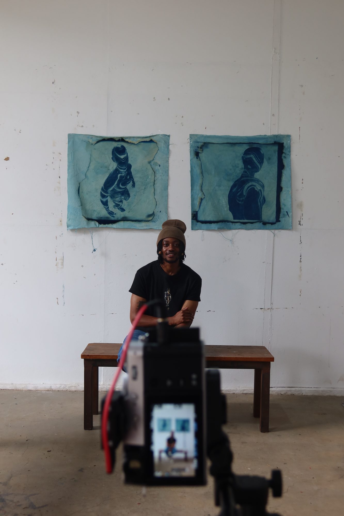 An artist filmed in front of two blue cyanotype works
